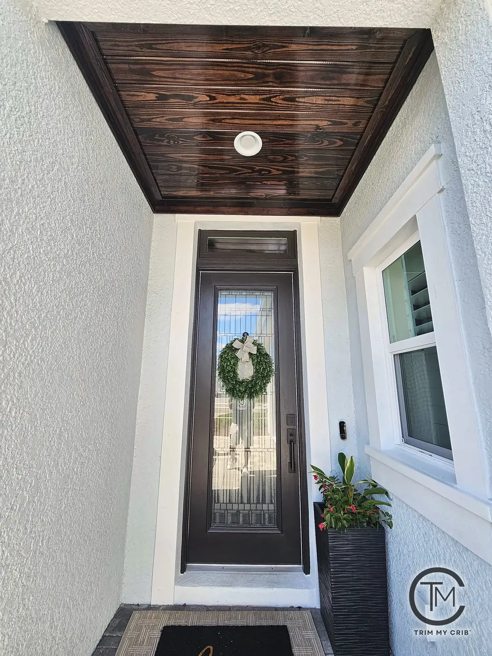 Front entry porch with a dark stained wood ceiling, recessed light and a tall glass front door