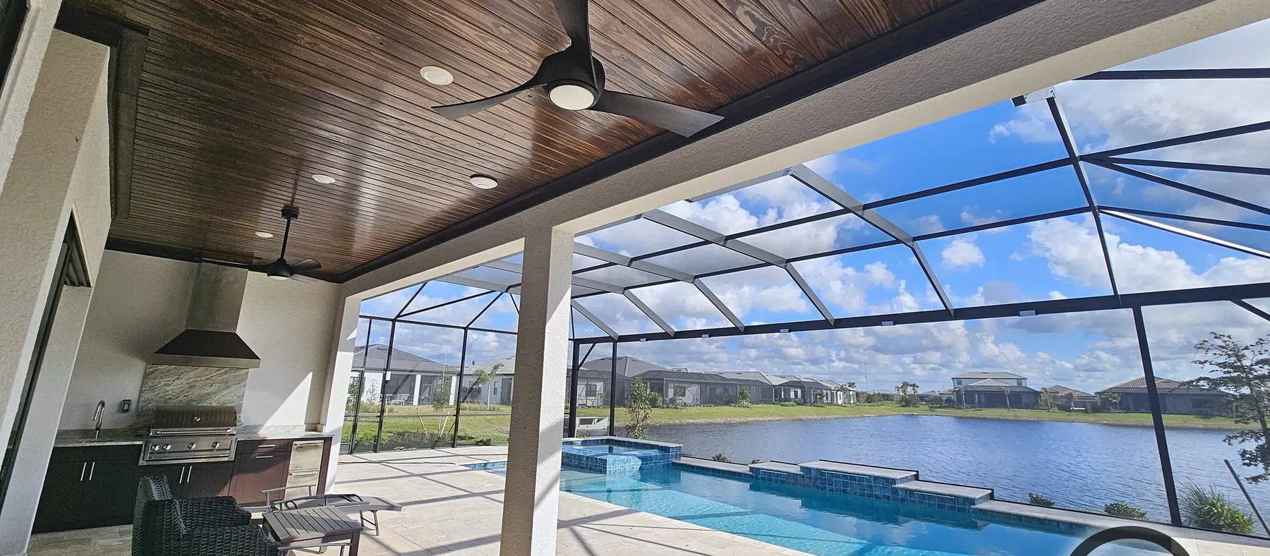 Pool lanai with a stained tongue-and-groove wood ceiling and black ceiling fan, looking out through the screen cage to the pool and lake
