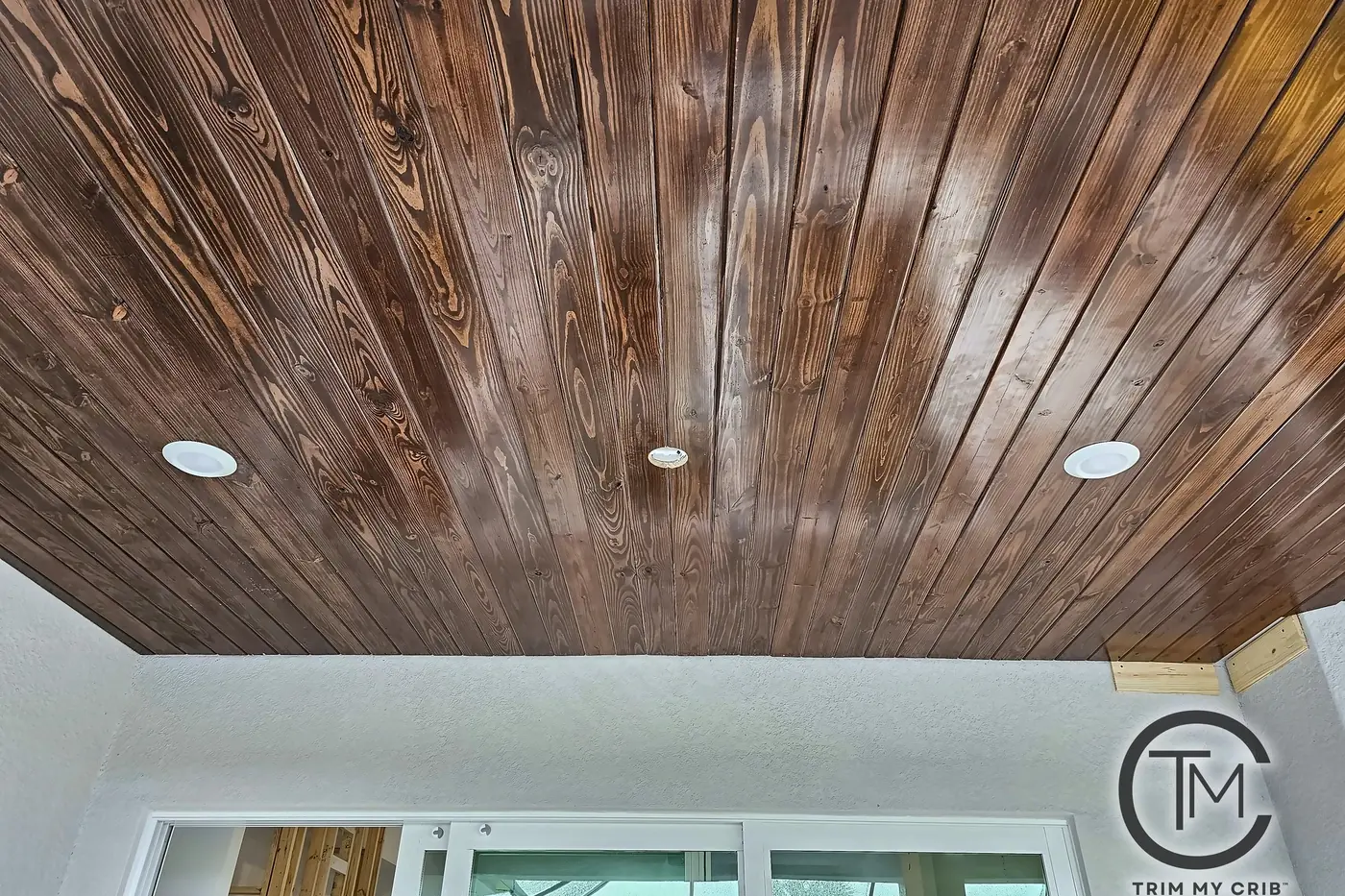 Close view of a stained wood porch ceiling with tight board joints and two recessed lights